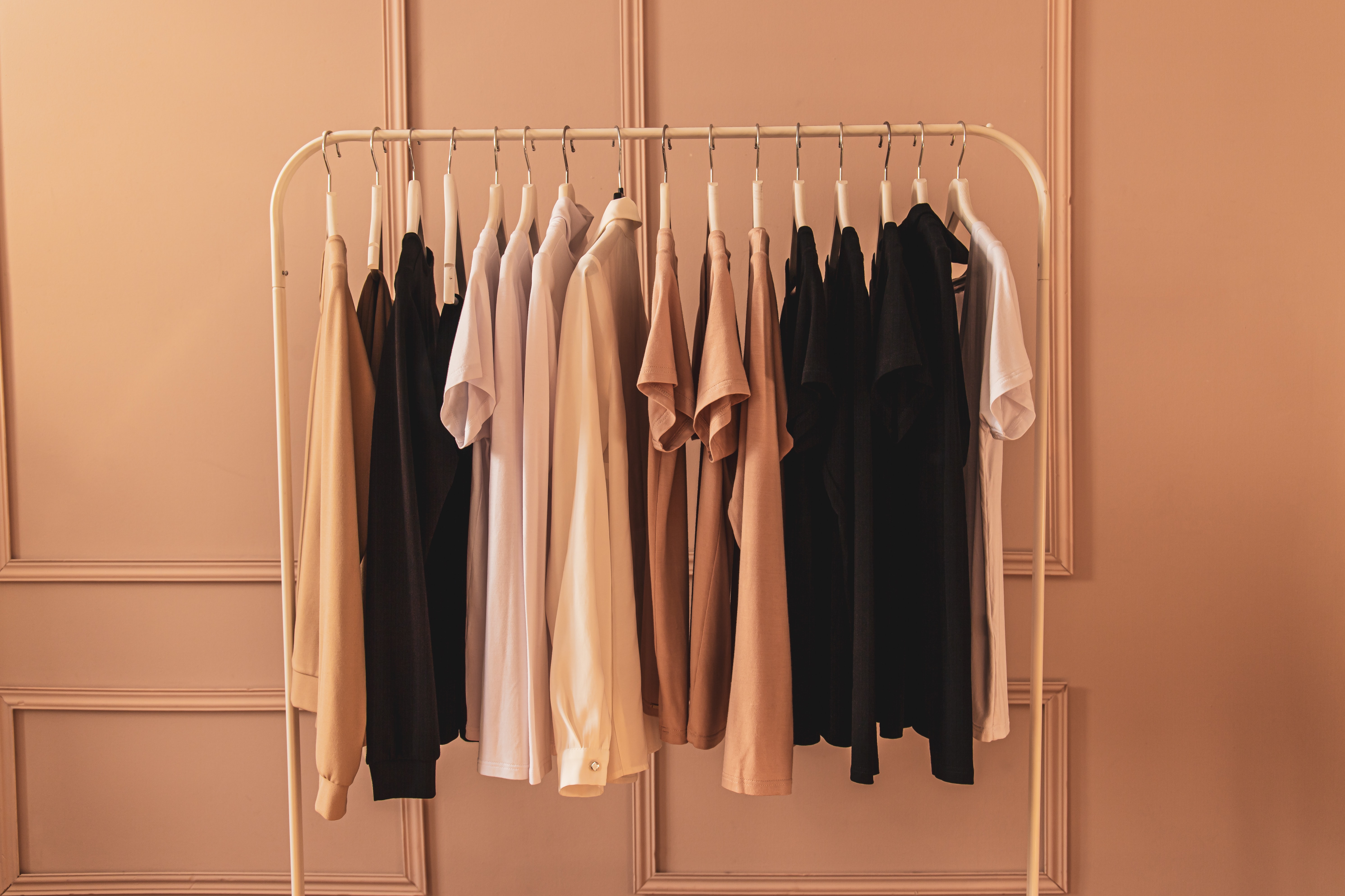 clothing rack of beige and black clothes against a beige, paneled wall. 